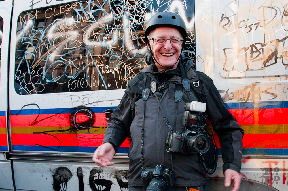 Photographer David Hoffman wearing protective helmet and bullet proof vest in front of a police riot van