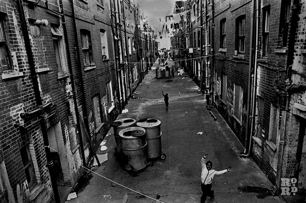 Black and white photo of Asian boy dancing in the streets, East End slums, by David Hoffman