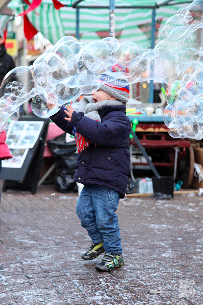 Boy laughing and trying to catch giant bubbles in outdoor street market.
