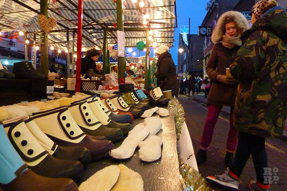 Market stall selling ankle wet weather boots, at dusk lit by festoon lighting.