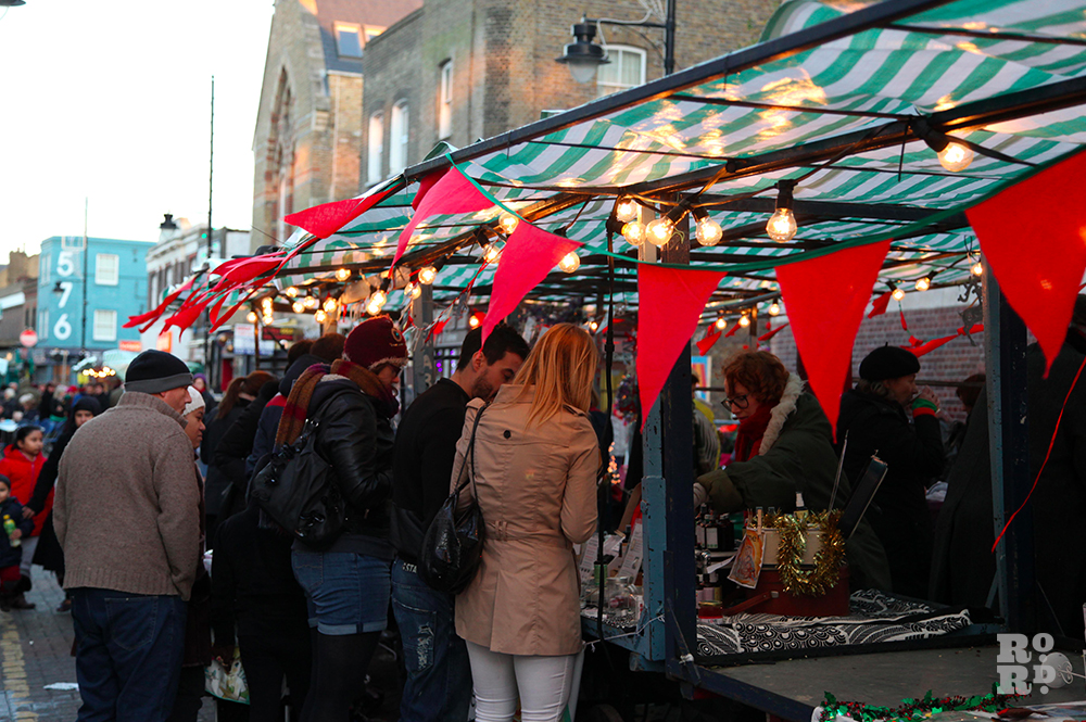 Red bunting flying in wind with festoon lighting on market stall with green and white tarp.