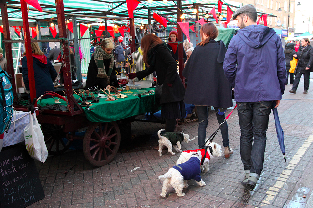 Man with small white dogs walking past market stalls
