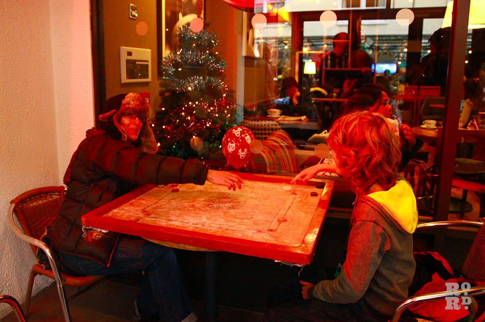 Woman and boy playing carrom outside a cafe on a cold day.
