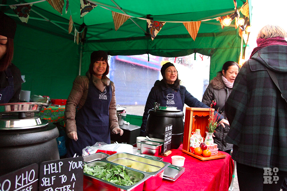 Laughing Vietnamese women selling street food from green gazebo with bunting.