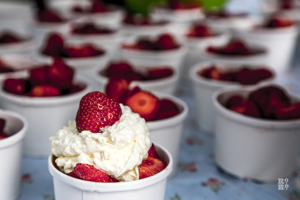 Rows of cardboard cups filled with strawberries and squirty cream