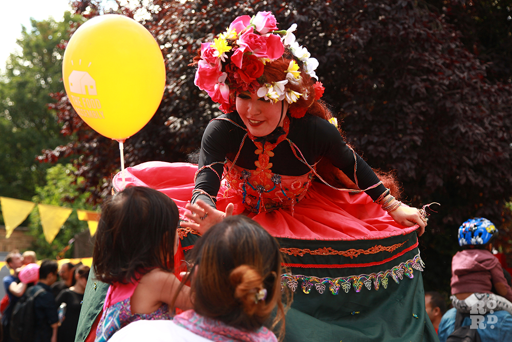 Ramanaya stilt walker talking to child with yellow balloon at Roman Road Festival