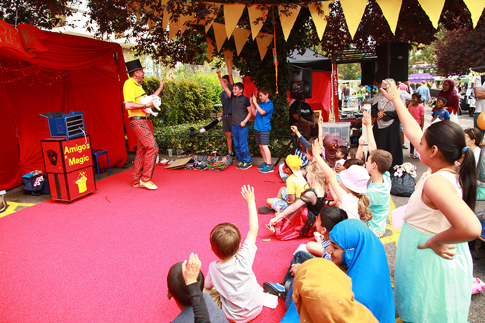 Magician on red carpet with children holding up hands, village fete bunting