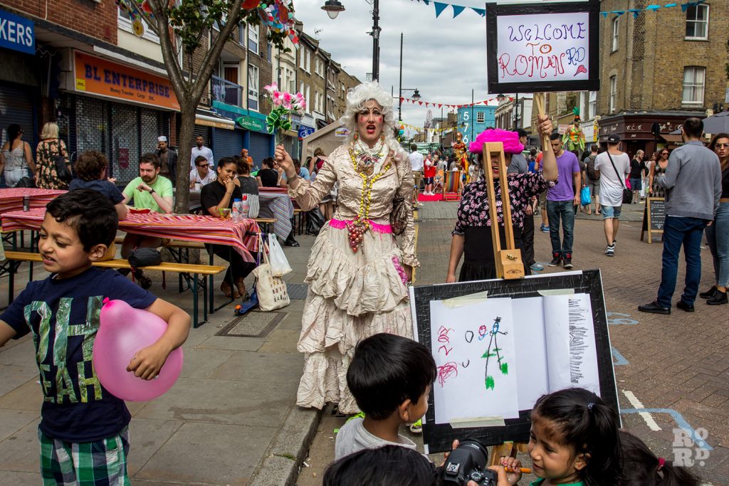 Performers in fancy dress bearing a placard saying Welcome to Roman Road at Roman Road Summer Festival 2016