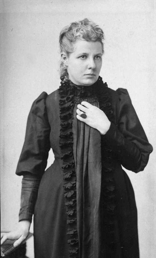 Blakc and white photograph of Annie Besant in a black dress looking stately.