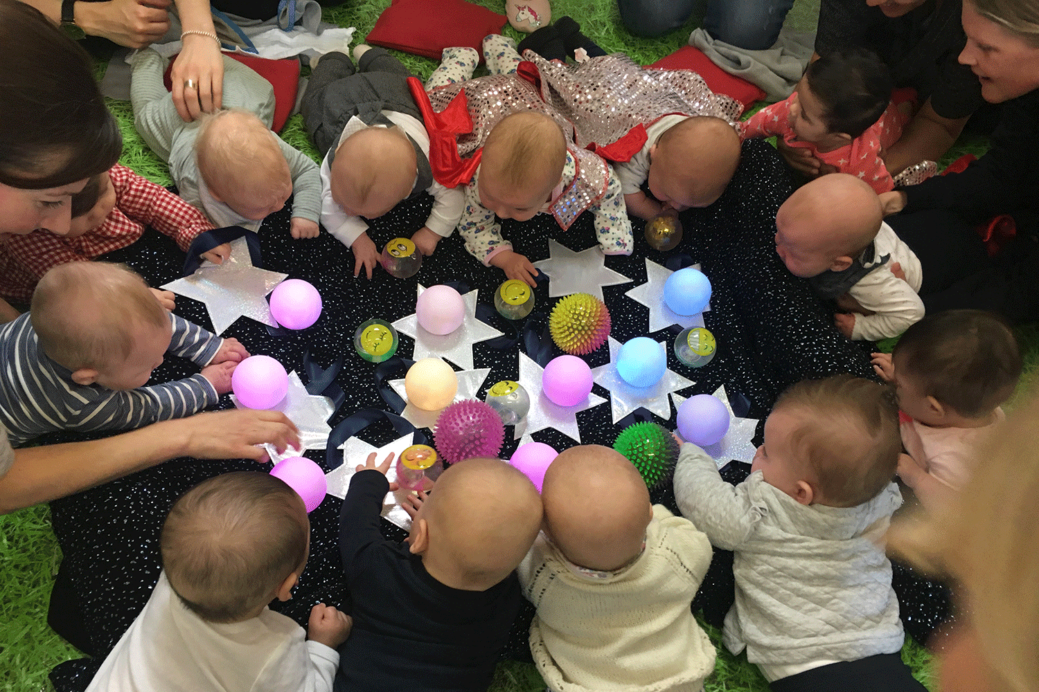 Babies held by parents around a table with cut out paper stars and different balls at Hartbeeps in Victoria Park, East London