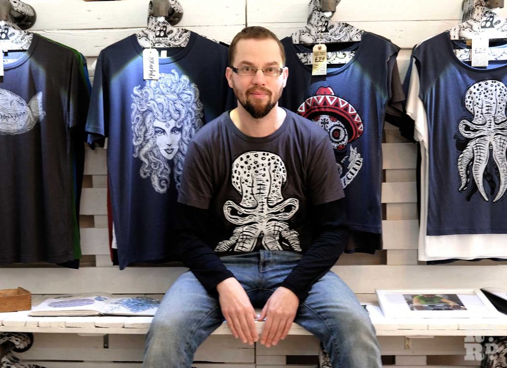Designer sits in front of his T shirt collection in Bamboo and Bee store