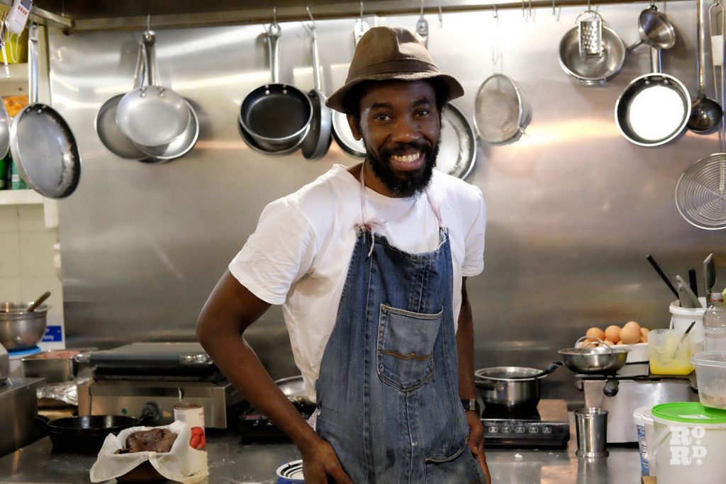Man wearing hat and apron stands in stainless steel industrial style kitchen
