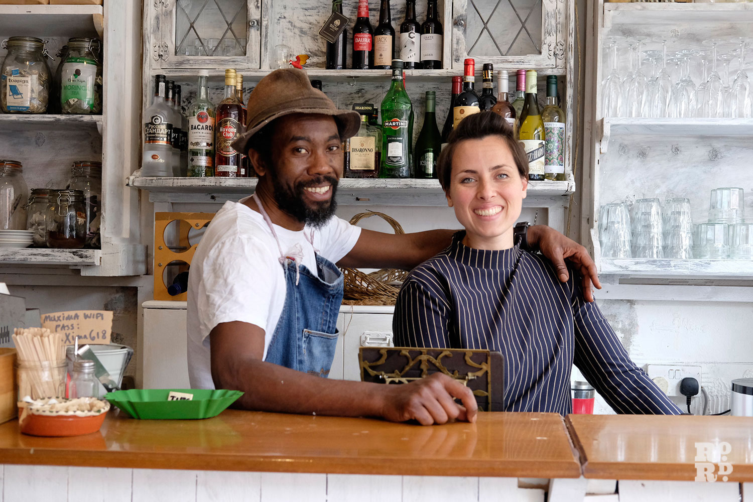 Co-owners of Muxima restaurant stand behind deli counter smiling