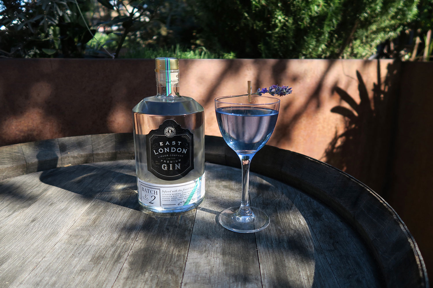 Bottle of gin on garden table next to cocktail in blue glass