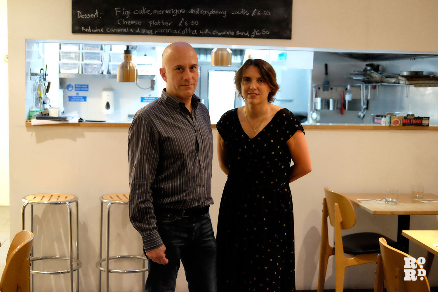 A man and a woman stand in front of the kitchen inside a restaurant