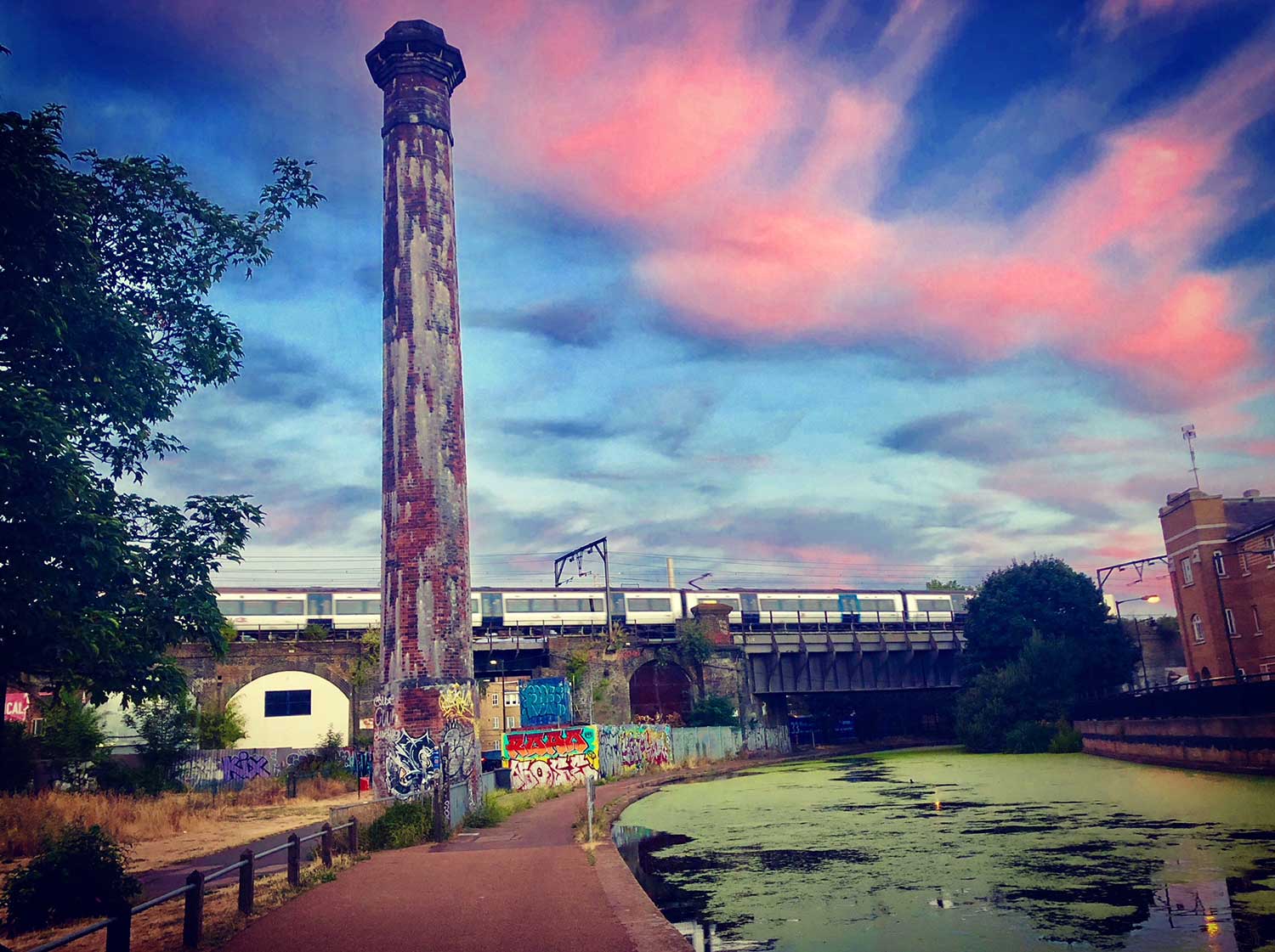 Brick tower by algae covered canal with dramatic sky