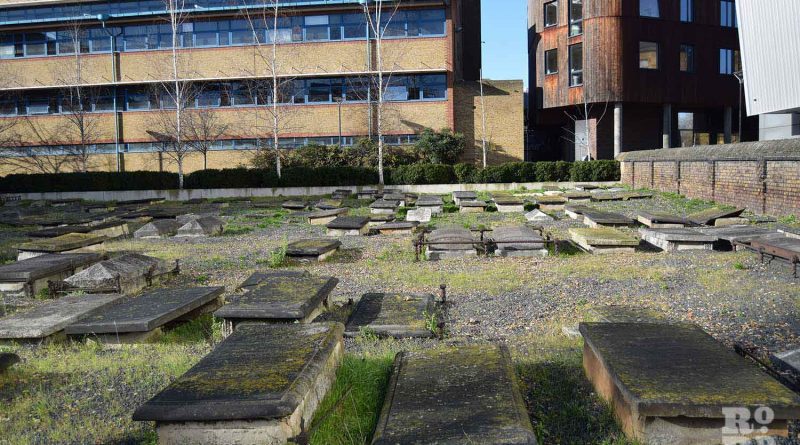 Many horizontal gravestones with Queen Mary university buildings in the background at Novo Jewish Cemetery, Mile End, London.