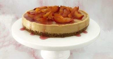 Photo of a white chocolate and biscoff cheesecake topped with a nectarine fruit compote and syrup on a white circular cake stand