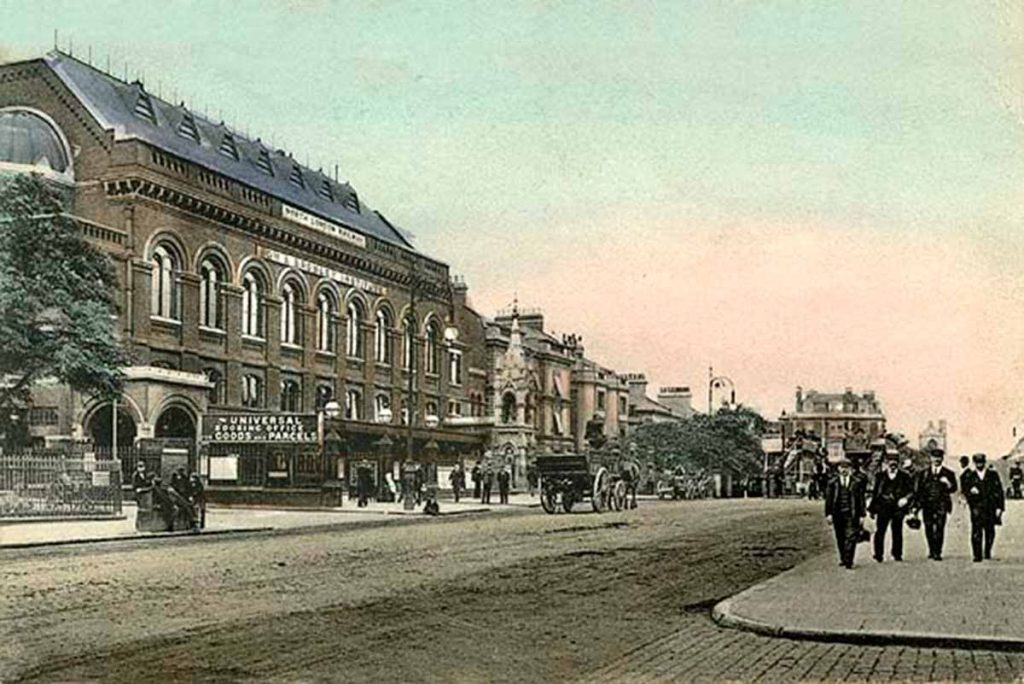 Coloured postcard from 1904 depicting Bow Station, its concert hall and the Bryant & May tribute fountain