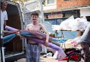 A man with his shirt off holds rolls of fabric at Roman Road Market photoessay from 2020, by photographer Wedgley Snipes.