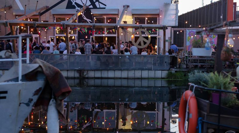 Multi-coloured fairy lights over a busy pub by a canal in Hackney Wick, East London