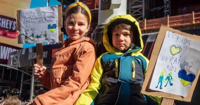 two young children holding up anti-war protest cards for Ukraine