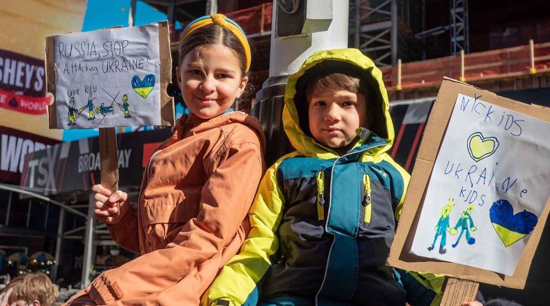 two young children holding up anti-war protest cards for Ukraine