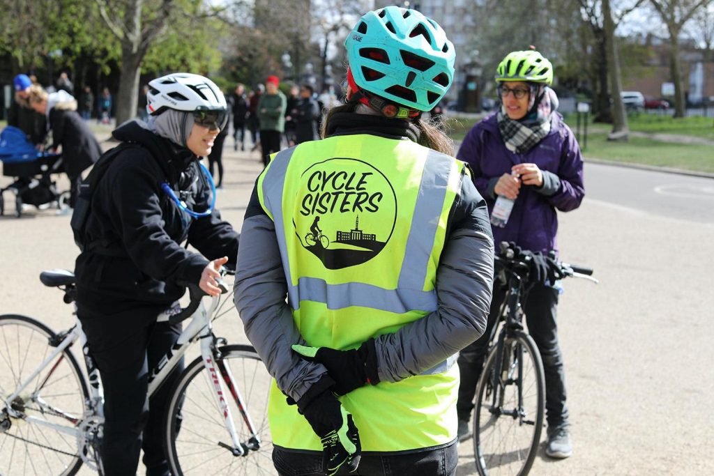 A woman with her back to the camera in a Hi Vis jacket with 'Cycle Sisters' logo