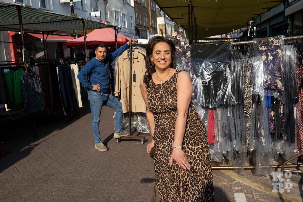 Woman in a leopard printed dress sitting in the Roman Road market, with a market stall holder standing behind here, Bow, East London