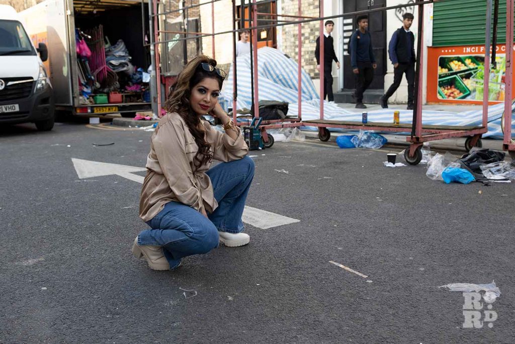 Woman posing on the road with Roman Road market behind her, Bow, East London