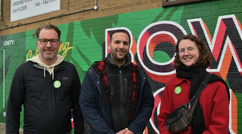 Three people with green party badges on standing in front of building in Bow, East London