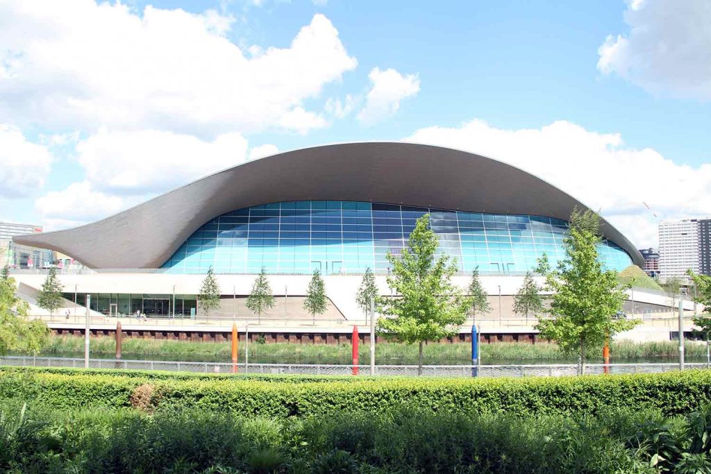 The London Aquatics centre, surrounded by grass and trees.