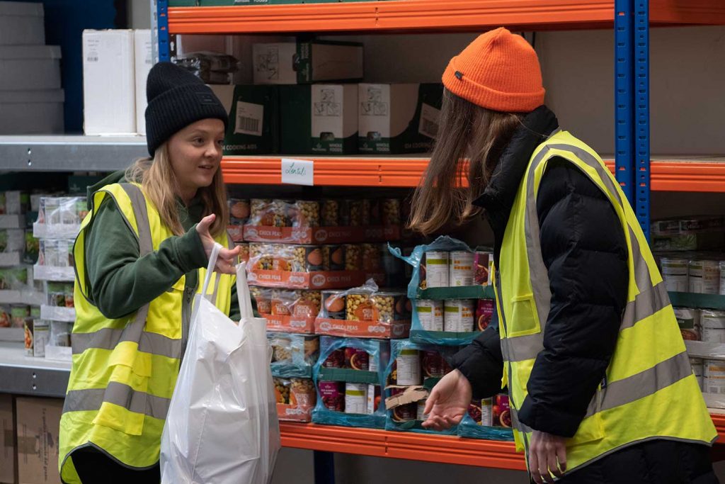 woman in hi-vis jacket handing a shopping bag to another woman in Bow Foodbank, Bow, East London