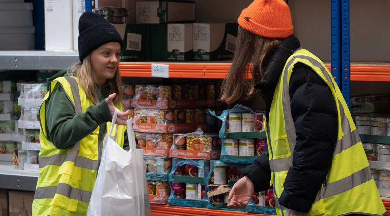 woman in hi-vis jacket handing a shopping bag to another woman in Bow Foodbank, Bow, East London