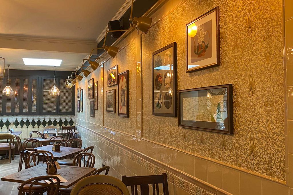 the interior of The Coborn with new light coloured tiles, art deco wall paper and pictures on the wall at The Coborn, Mile End, East London