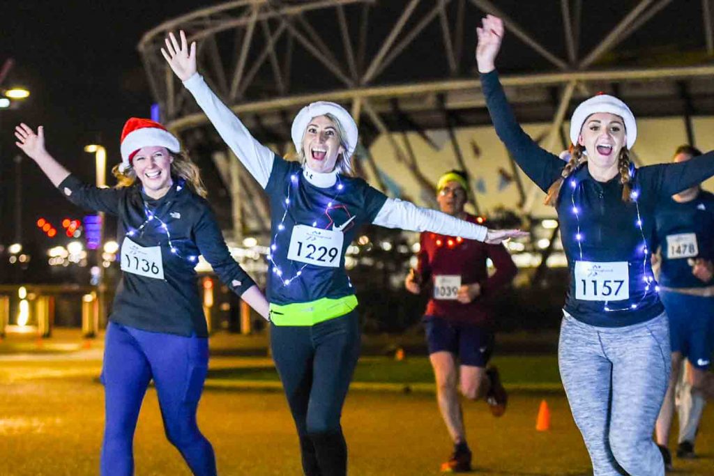 Three runners in Santa hats outside of the Queen Elizabeth Olympic stadium.