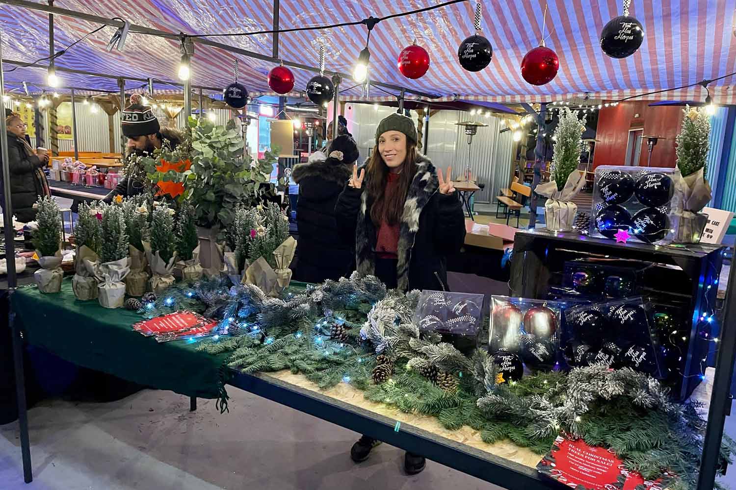 Woman standing behind stall at Hackney Wickmas selling Christmas tree decorations.