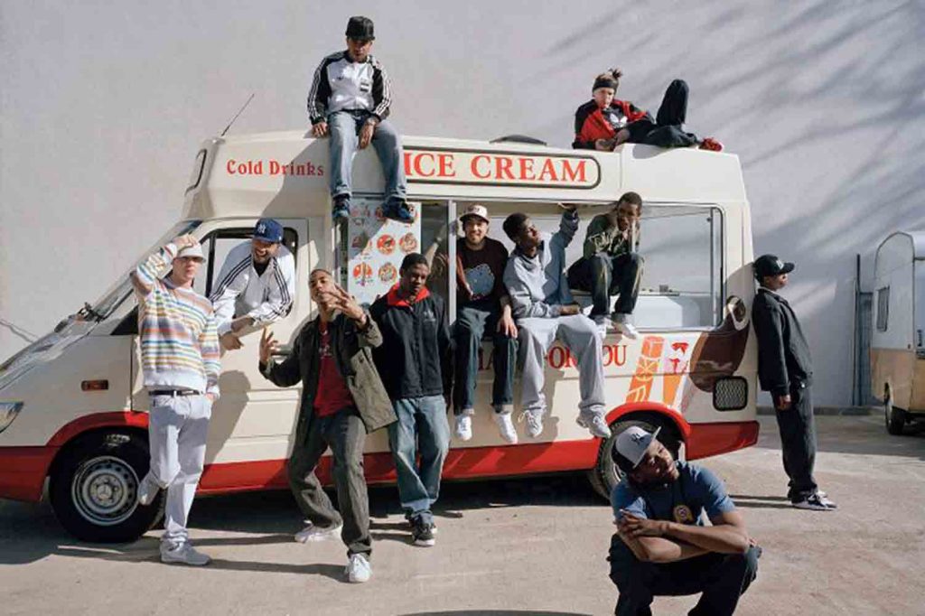 Photograph of grime rapper Wiley by an ice cream van with his entourage of ten.