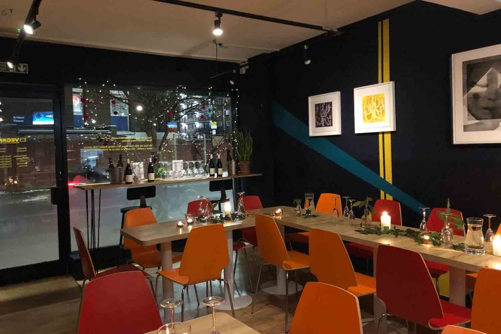 Interior of E3 Vegan Cafe with colourful chairs and wooden tables and a dark navy interior on Roman Road.