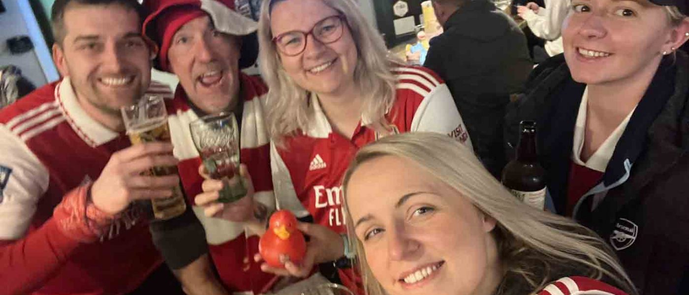 Arsenal women's legend Lotte Wubben-Moy surrounded by fans with pints, a red rubber duck and a TV in the background.