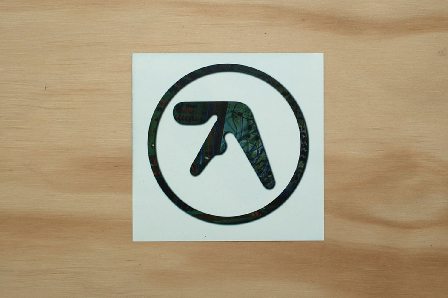 Aphex Twin's trademark logo with a wooden background