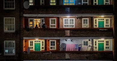 A block of flats with green doors in Whitechapel, East London, showing a courier delivering food at one of the apartments, and laundry hanging outside another. Photography by Matt Payne.