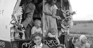 A group of Irish Travellers sat and stood at the back of a traditional carriage.
