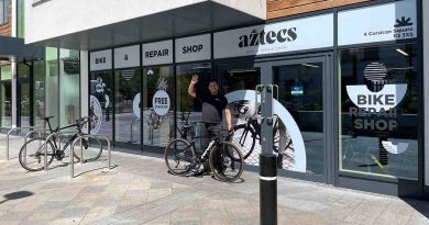Man waving with a bike outside a bike shop called aztec's bike and repair shop