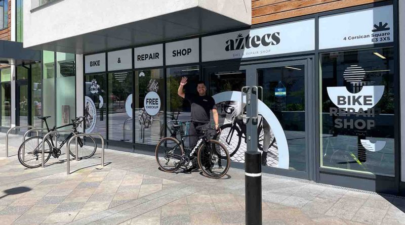 Man waving with a bike outside a bike shop called aztec's bike and repair shop
