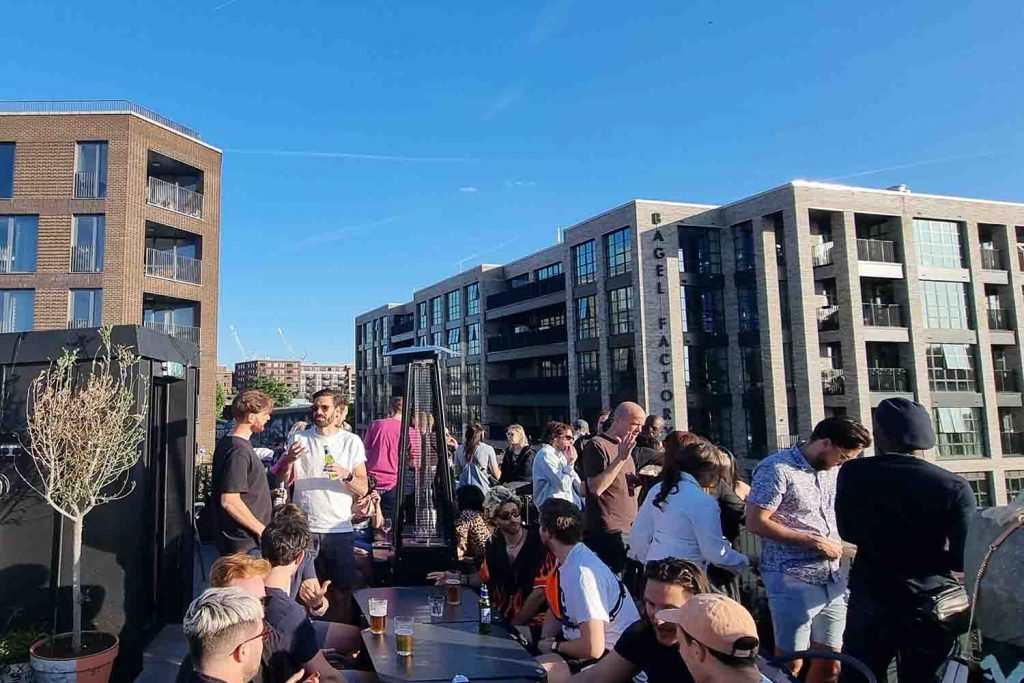 Busy rooftop bar in the sunshine with views of tall modern buildings.