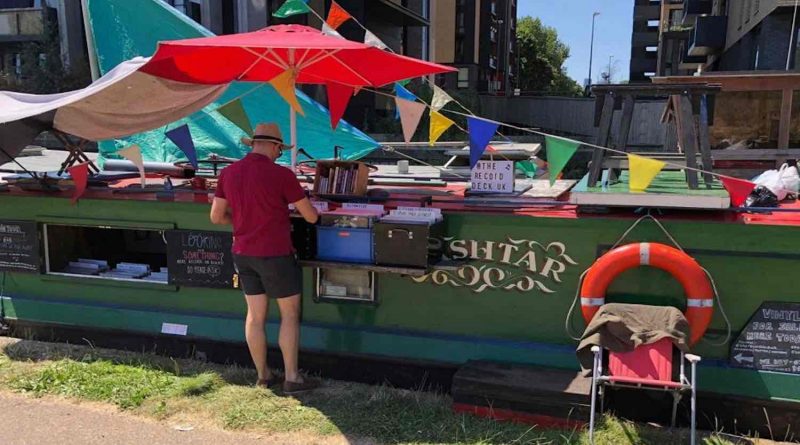 Man browses through records at a record shop that is a barge in the sun.