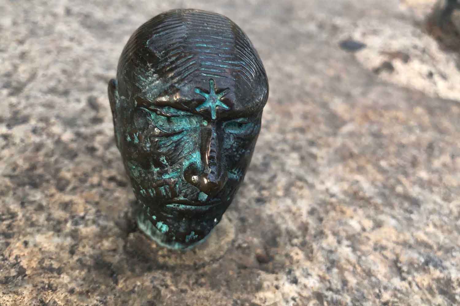 small bronze sculture of a head with a star on attached to a piece of stone.