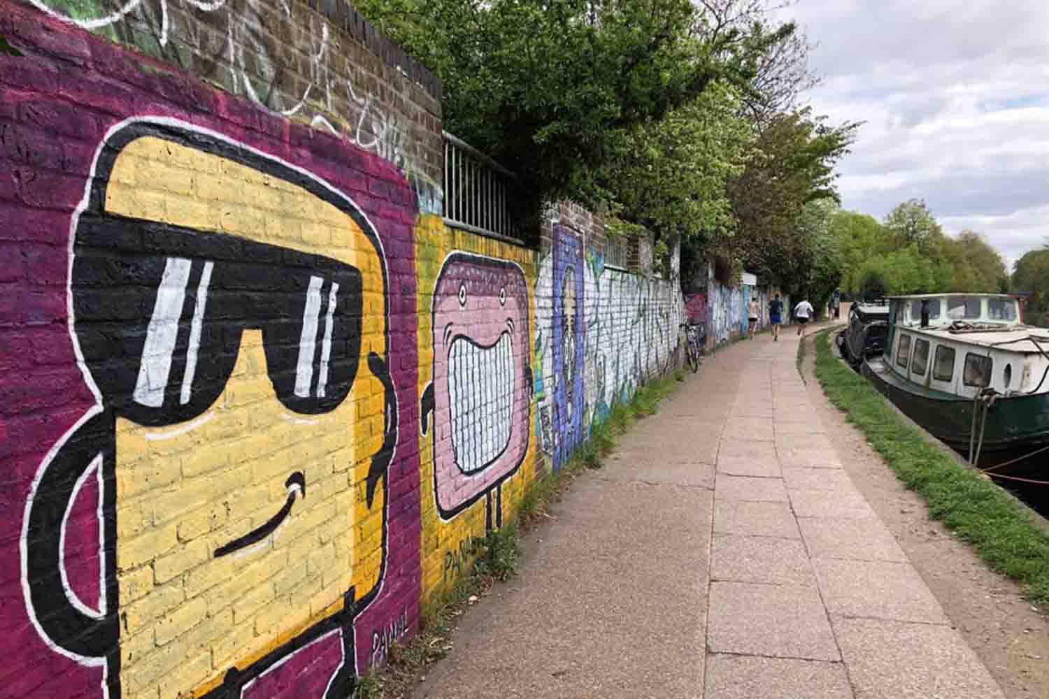 A wall lining a canal with street art depicitng cartoon-style figures.