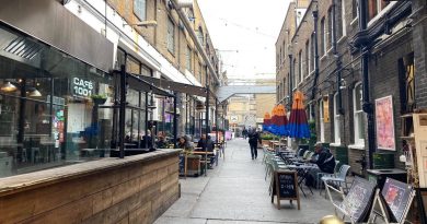 View down Dray Walk, Brick Lane, with outdoor seating and umbrellas.